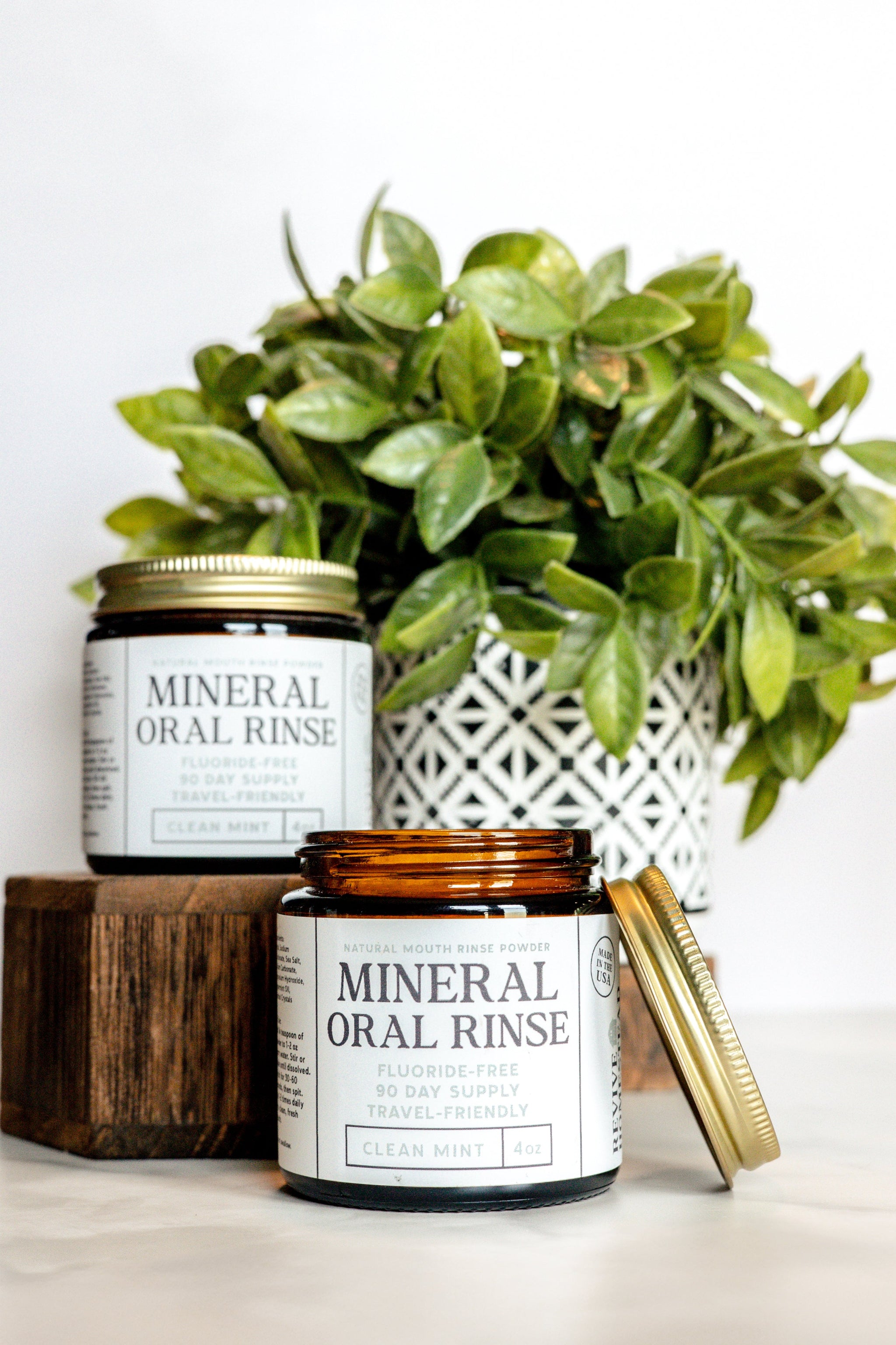 Two jars of fluoride-free mineral oral rinse powder sit near a potted plant, showcasing natural dental care.
