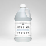 A bottle of Rustic Strength Rinse Aid displays its hypoallergenic and biodegradable formula, promising spotless, sparkling dishes with a short dry time.
