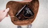 Person opens a brown leather bag revealing a laptop, camera, and leather pouch inside.
