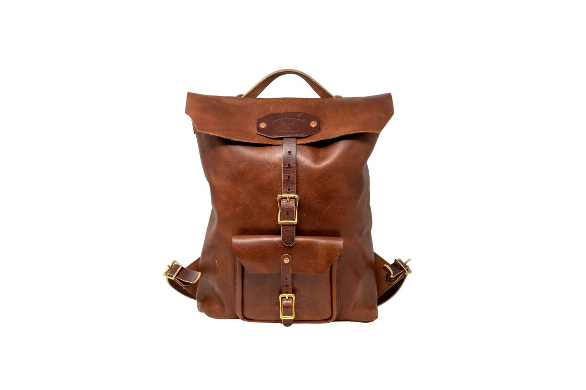 A vintage-style leather backpack with brass buckles sits against a white backdrop.
