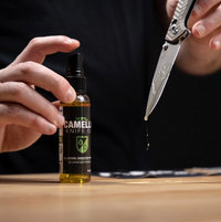 Camelot Knife Oil bottle with a hand applying oil to a knife blade.