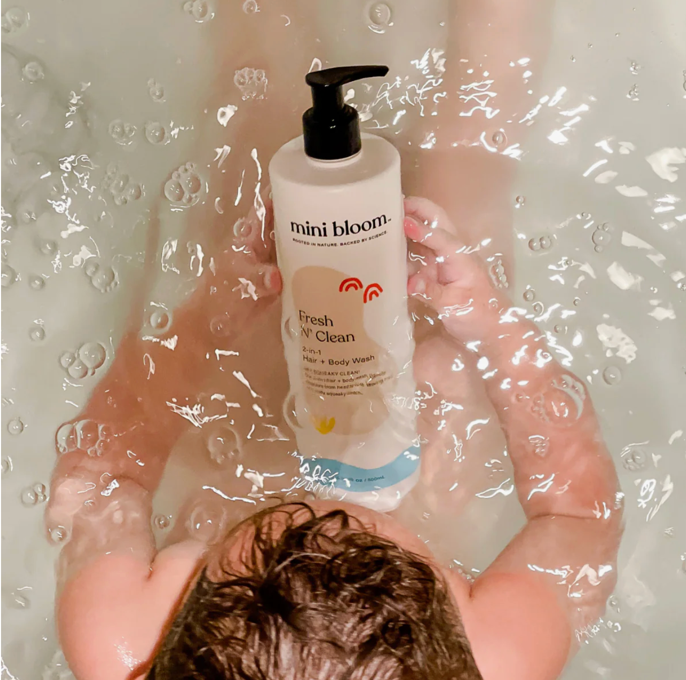 Child holding a Mini Bloom hair & body wash in the bathtub.