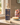 A bottle of Cristina's Curls Kids Curl Enhancing Hair Oil Collection stands on a wooden windowsill with warm natural light. The bottle has a dark navy blue label with gold and white text and illustrations.