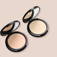 Two open compacts display light beige face powder with mirrors inside black cases.

