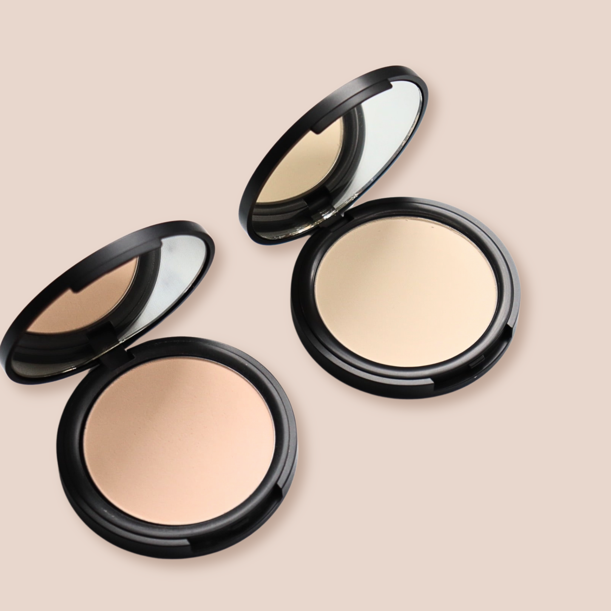 Two open compacts display light beige face powder with mirrors inside black cases.

