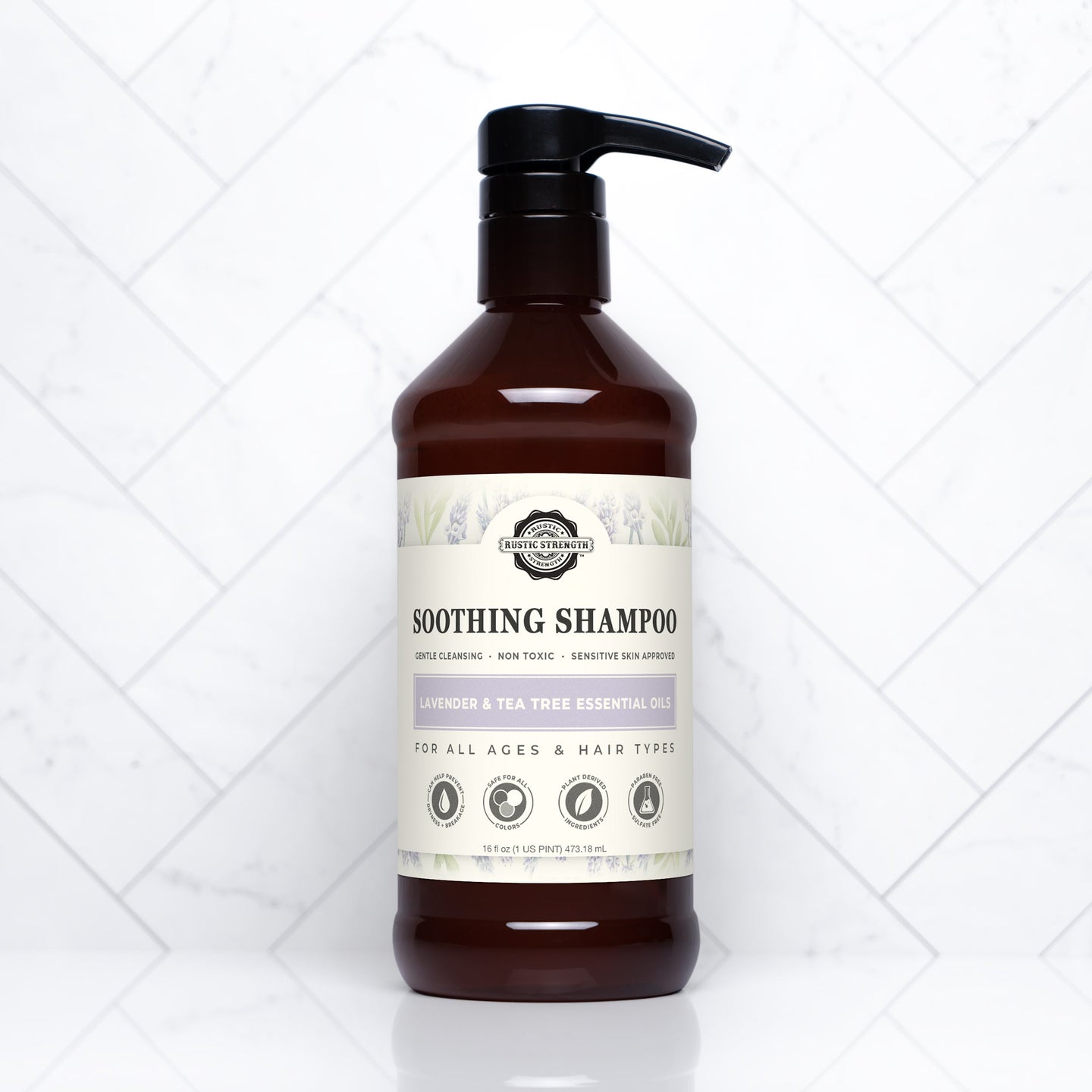 A brown bottle of Rustic Strength Soothing Shampoo with lavender and tea tree essential oils sits on a white tile surface.
