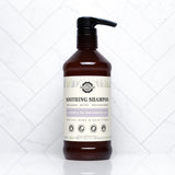 A brown bottle of Rustic Strength Soothing Shampoo with lavender and tea tree essential oils sits on a white tile surface.
