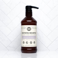A brown bottle of Rustic Strength Soothing Shampoo with lavender and tea tree essential oils sits on a white tile surface.
