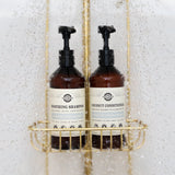 Shower water streams over Rustic Strength's unscented, hypoallergenic soothing shampoo and coconut conditioner set for all hair types, displayed in a gold shower caddy.
