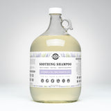 A one-gallon glass jug contains Rustic Strength Soothing Shampoo with lavender and tea tree essential oils, marketed as gentle, non-toxic, and suitable for all ages and hair types.
