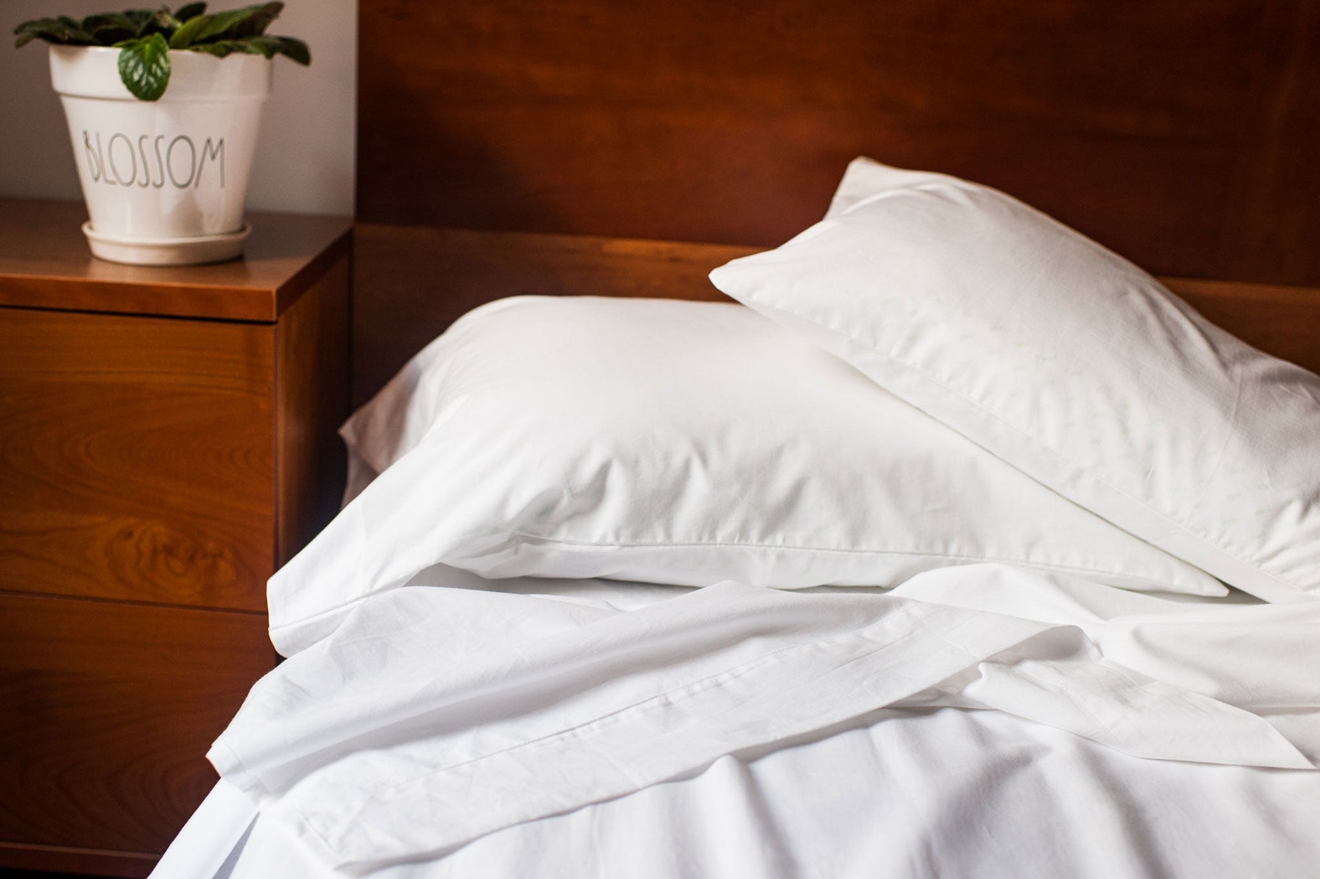 White bedding on a bed with a wooden headboard and nightstand.