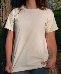 A woman models a soft cream-colored organic cotton t-shirt while standing near a tree.
