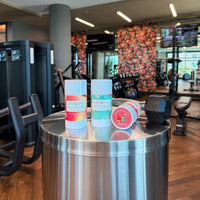 Breathe Naturals deodorants in strawberry colada, summer seabreeze, and watermelon scents sit on a table beside a dumbbell at the gym.
