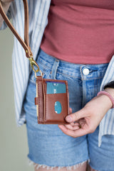 A person displays a brown leather card holder wallet with a lanyard attached.
