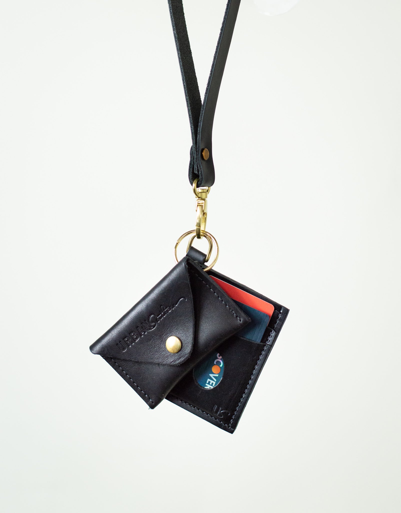 A black leather lanyard wallet holding credit cards hangs against a white background, showcasing convenient cardholder style.
