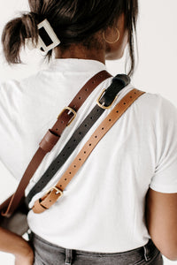 Woman models three leather belts with gold buckles in varying shades of brown and black, showcasing fashion accessories.