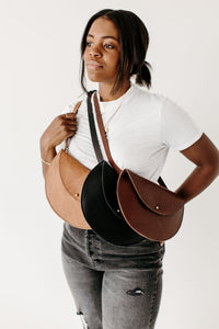 A Black woman models three different leather crossbody bags in tan, black, and brown.
