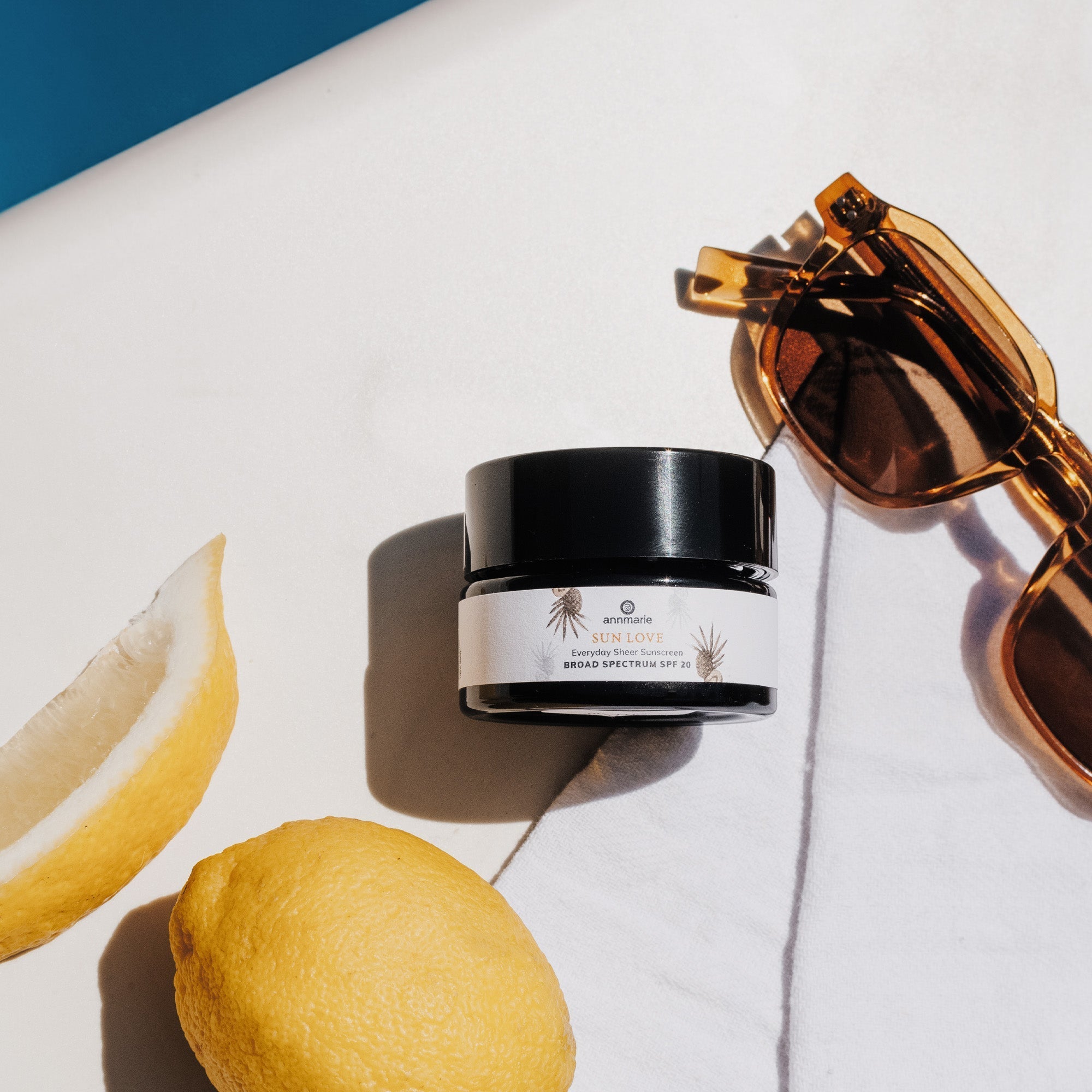Sunscreen sits with lemons and sunglasses on a white towel for a summer skincare promotion.
