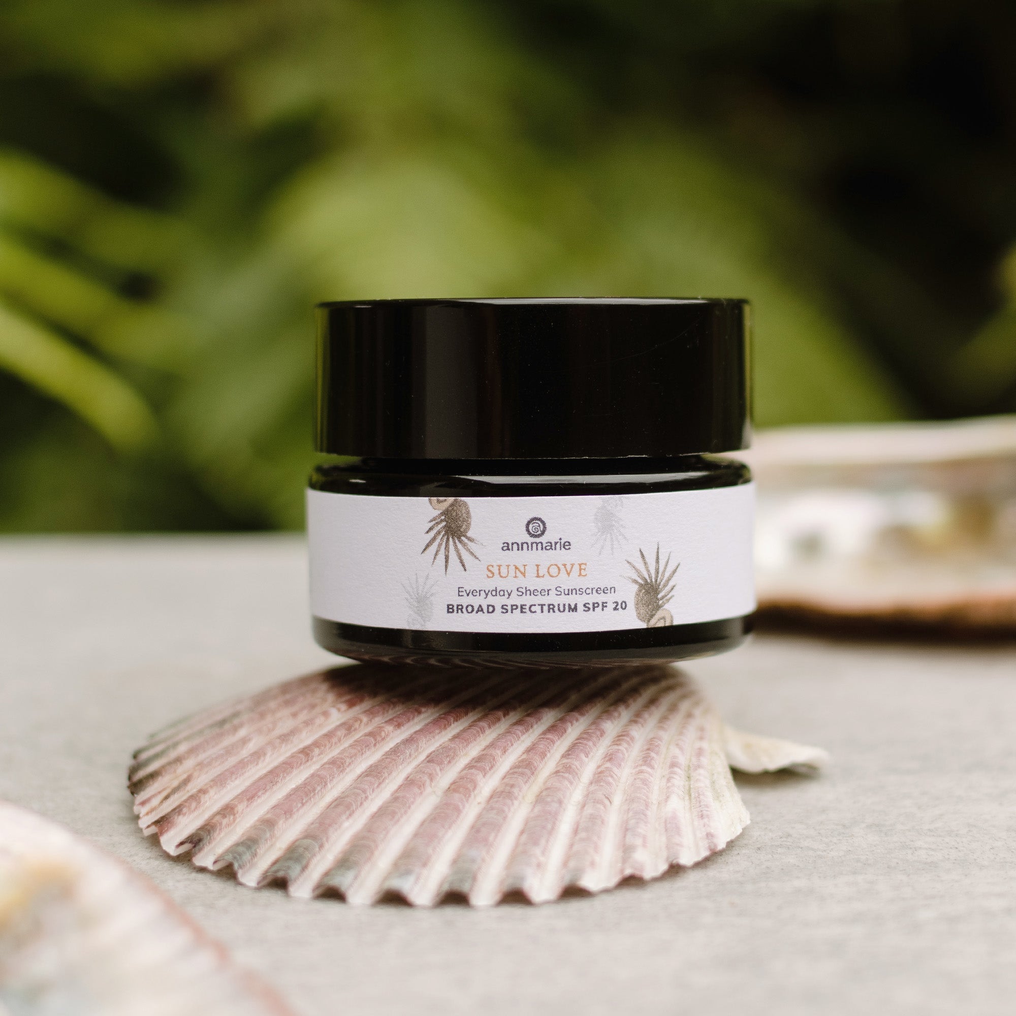 Annmarie Sun Love sunscreen sits on a seashell, advertising everyday sheer broad spectrum SPF 20 protection.

