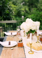 A beautifully styled outdoor dinner table features white hydrangeas, gold accents, and artisanal cocktails.

