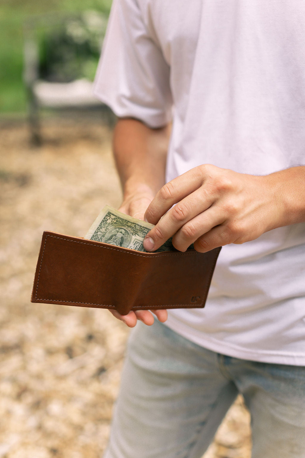 A man pulls a one-dollar bill from his brown leather wallet.
