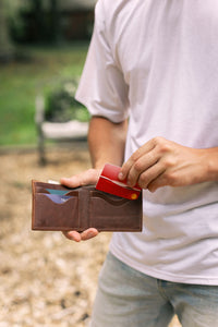 Man pulls a red credit card from a brown leather wallet outside.
