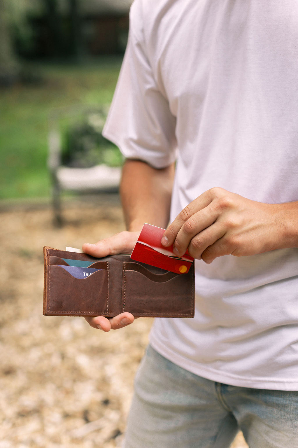 Man pulls a red credit card from a brown leather wallet outside.
