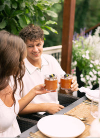 Couple cheers with refreshing summer cocktails, garnished with blackberries, during an outdoor garden party.
