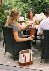 A woman grabs a chilled bottle from a leather wine cooler bag during an outdoor summer garden party.
