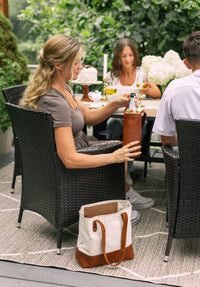 A woman retrieves a chilled wine bottle from a leather carrier while enjoying an outdoor gathering with friends and cake.

