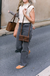Two women model handcrafted leather crossbody bags and tote bags while walking down a city street.
