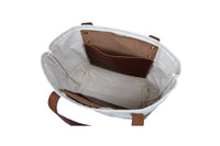 View shows the interior of a white canvas tote bag featuring brown leather pockets and straps.
