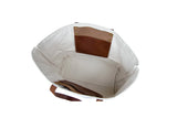 Open white canvas tote bag features brown leather straps and interior pockets.
