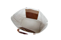 Open white canvas tote bag features brown leather straps and interior pockets.
