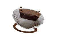 The canvas tote bag features brown leather handles and a convenient internal leather pocket.
