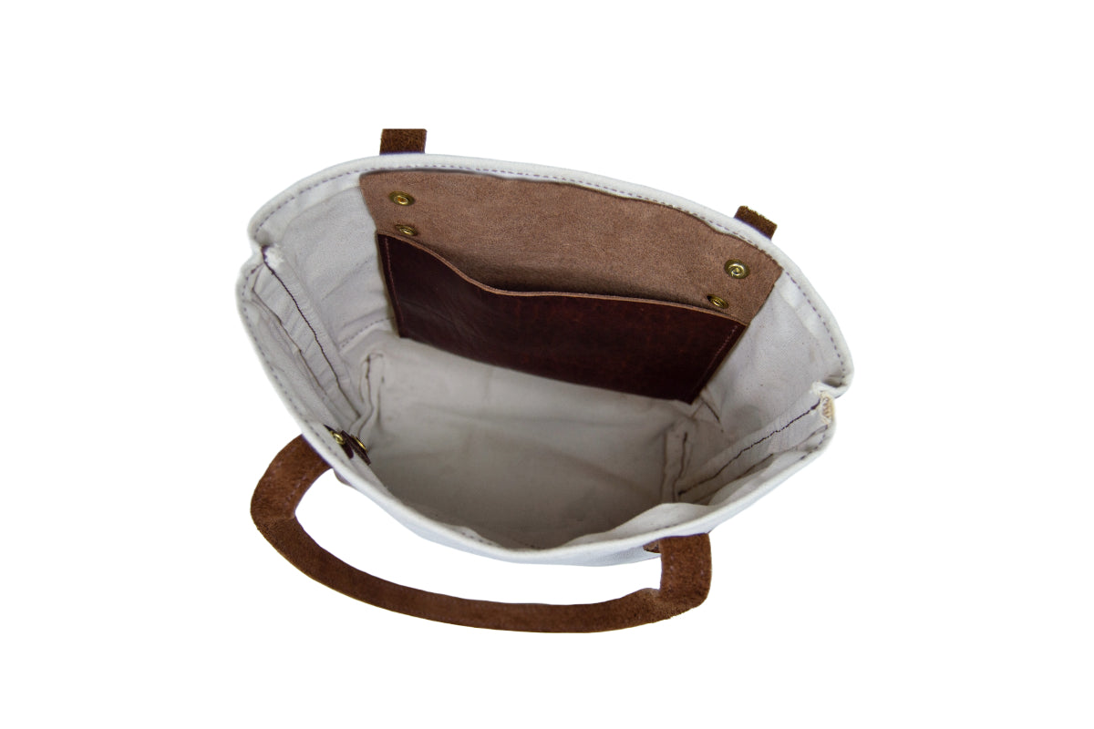 The canvas tote bag features brown leather handles and a convenient internal leather pocket.
