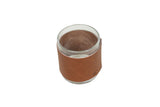 A clear glass candle holder sits encased in a brown leather sleeve.
