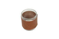 A clear glass candle holder sits encased in a brown leather sleeve.
