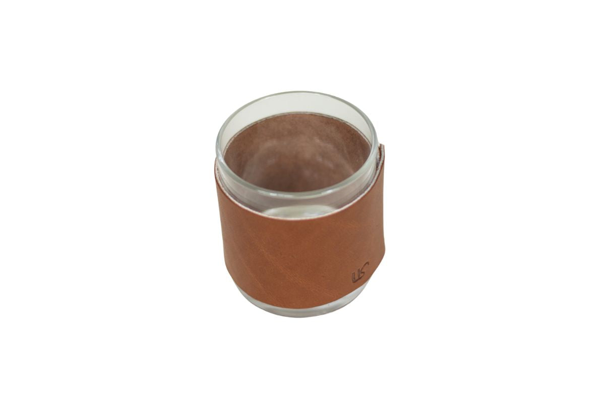 A clear glass candle holder sits encased in a brown leather sleeve.
