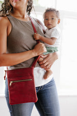 A mother carries her baby and wears a stylish red leather crossbody bag.
