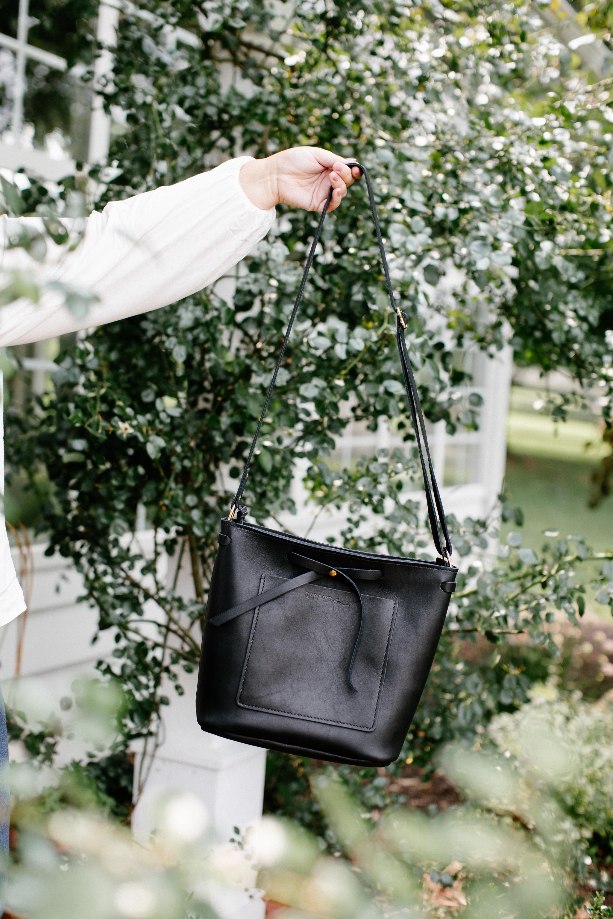 A person holds up a stylish black leather crossbody bag outdoors.
