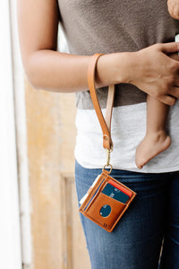 Mom carries her baby while showcasing a leather lanyard wallet with credit cards.
