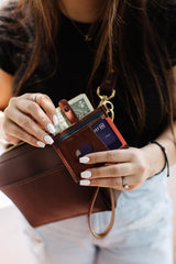 Woman pulls out cash and a debit card from a brown leather wallet attached to a crossbody bag.
