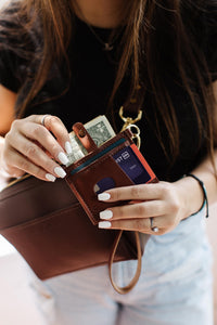 Woman pulls out cash and a debit card from a brown leather wallet attached to a crossbody bag.
