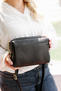 Woman models a black leather crossbody bag from Urban Southern, showcasing its design and stylish look.
