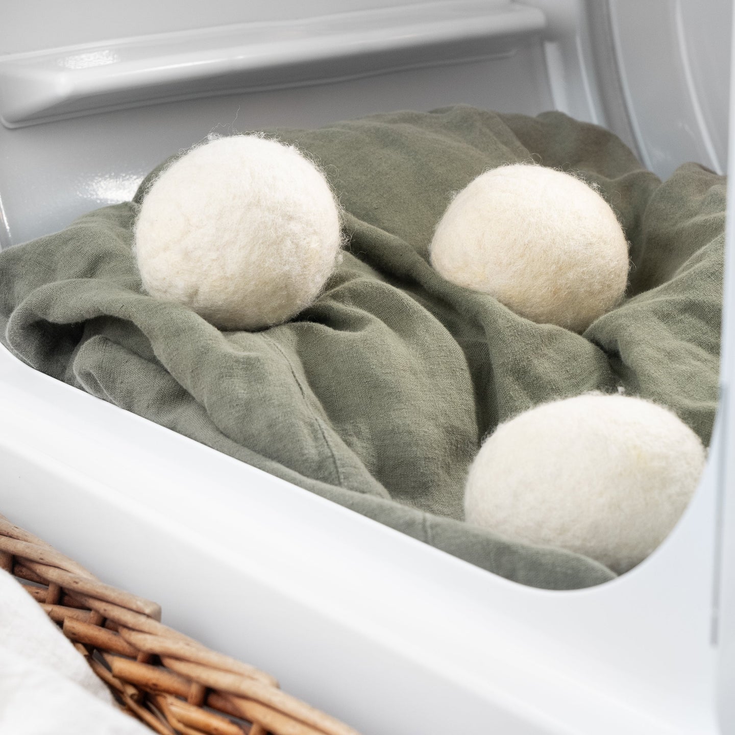 Three wool dryer balls tumble with olive-green fabric inside a white laundry dryer.
