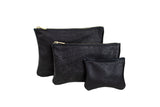Three black leather zip pouches, in graduating sizes, display their textured material and gold zippers.

