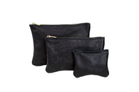 Three black leather zip pouches, in graduating sizes, display their textured material and gold zippers.
