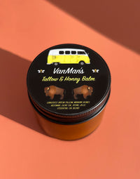 VanMan's Tallow & Honey Balm, featuring bison tallow and manuka honey, sits on a peach background and showcases a yellow van on its black label.
