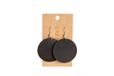 Display presents chic, round black leather earrings hanging on a branded retail card.

